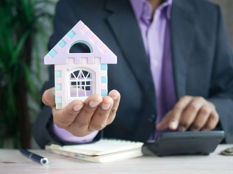 Persona haciendo cuentas con una calculadora junto a la maqueta de una casa