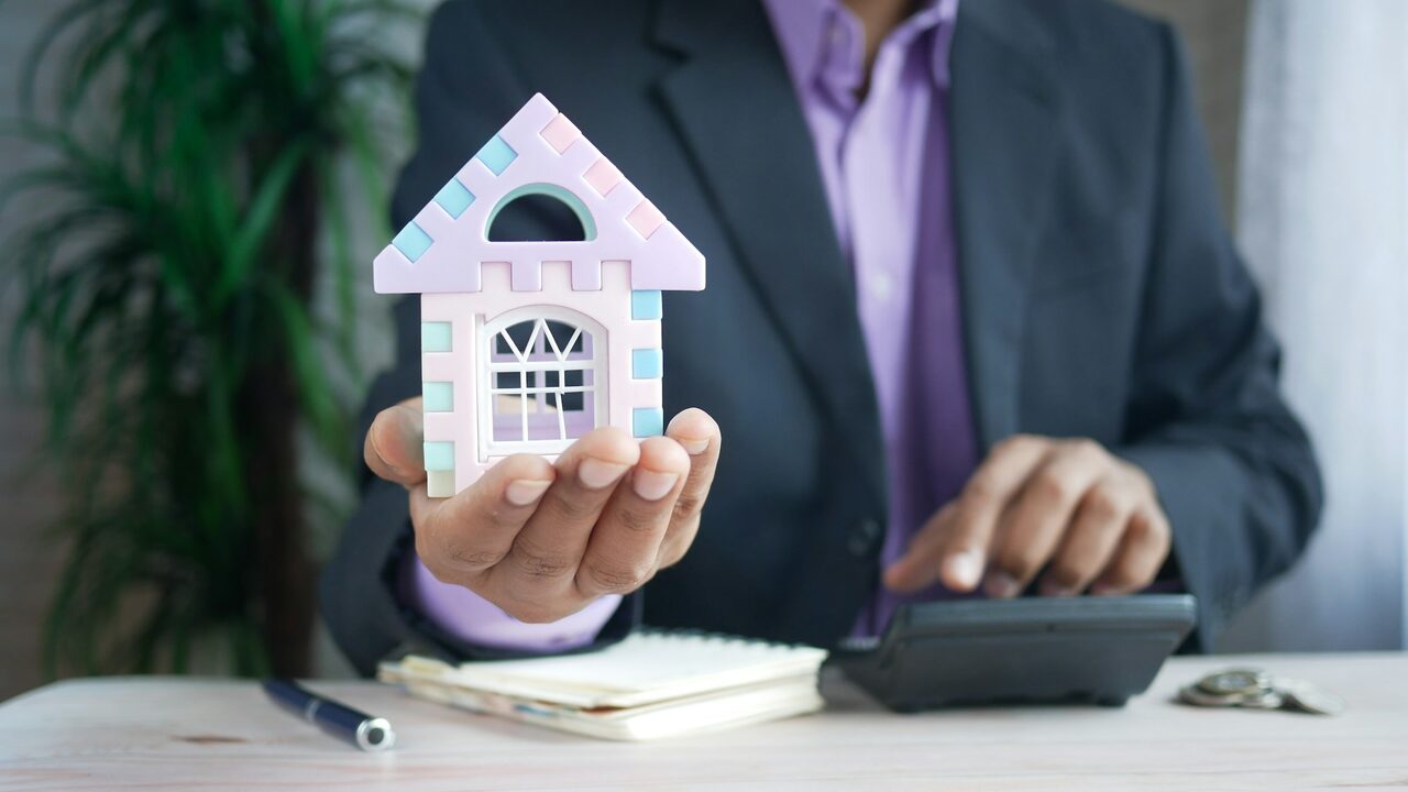 Persona haciendo cuentas con una calculadora junto a la maqueta de una casa
