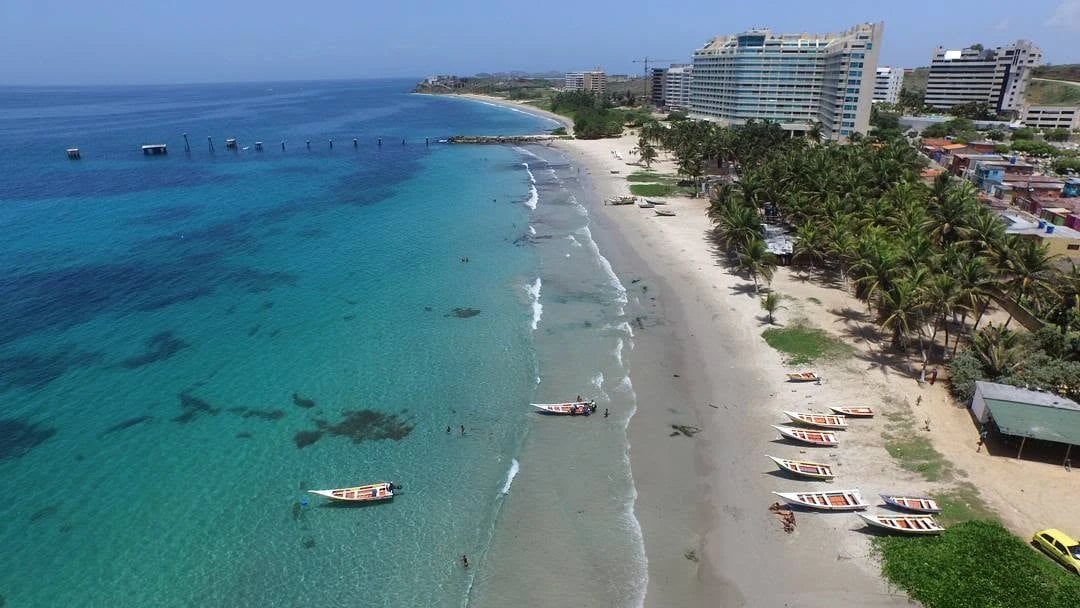Vista aérea de la bahía de Pampatar, en la Isla de Margarita, con peñeros en la arena, palmeras y hoteles frente al mar